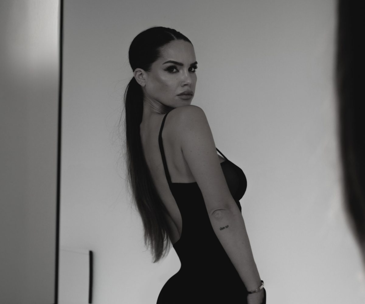 Woman hiker with backpack standing on country path with her hands outstretched and bright sunlight from back. Female hiker feeling happy during a hike.